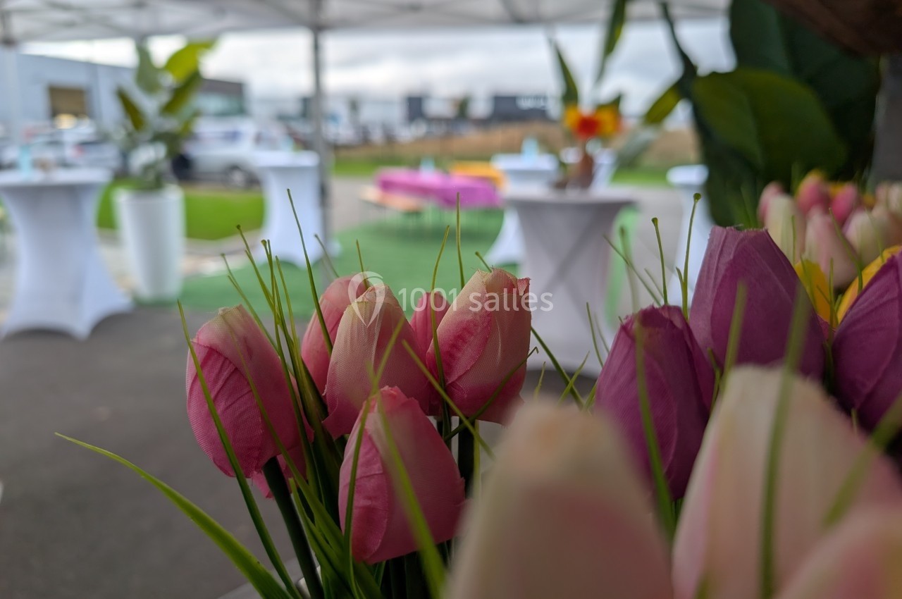 Tulipes roses et blanches au premier plan, avec des tables hautes et un espace extérieur flou en arrière-plan.