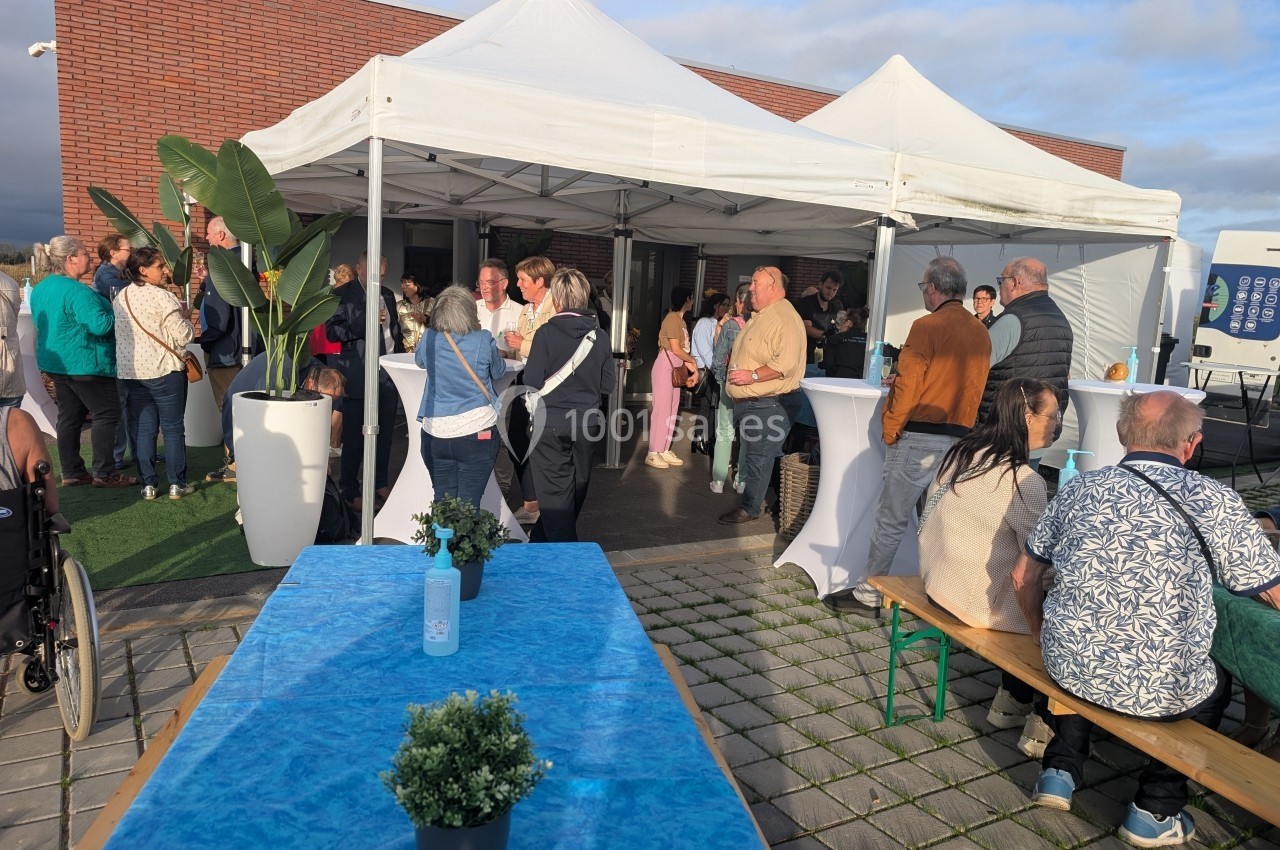 Groupe de personnes rassemblées sous des tentes blanches lors d'un événement en extérieur, avec tables et plantes…