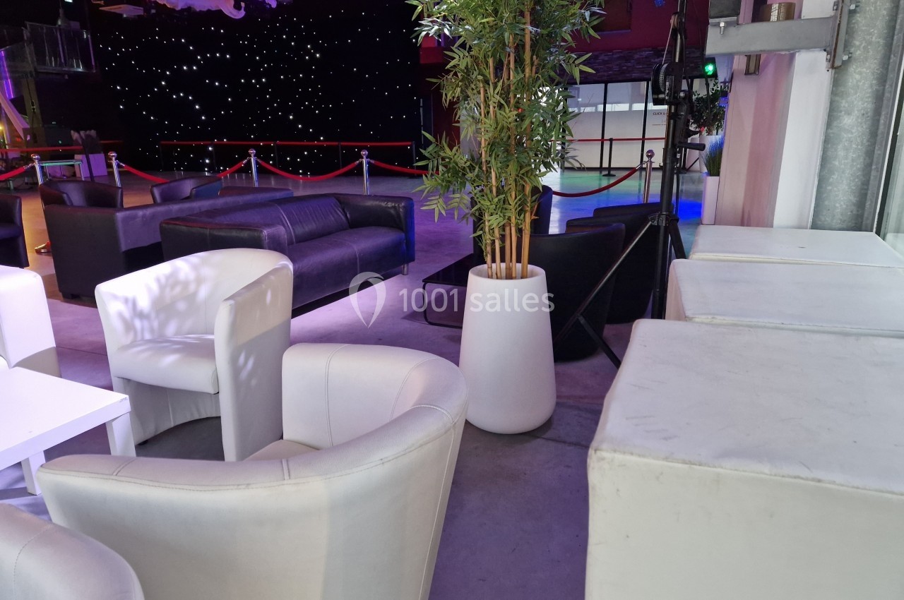 Espace intérieur avec fauteuils blancs, canapé noir, plantes en pot et éclairage tamisé devant un fond étoilé.