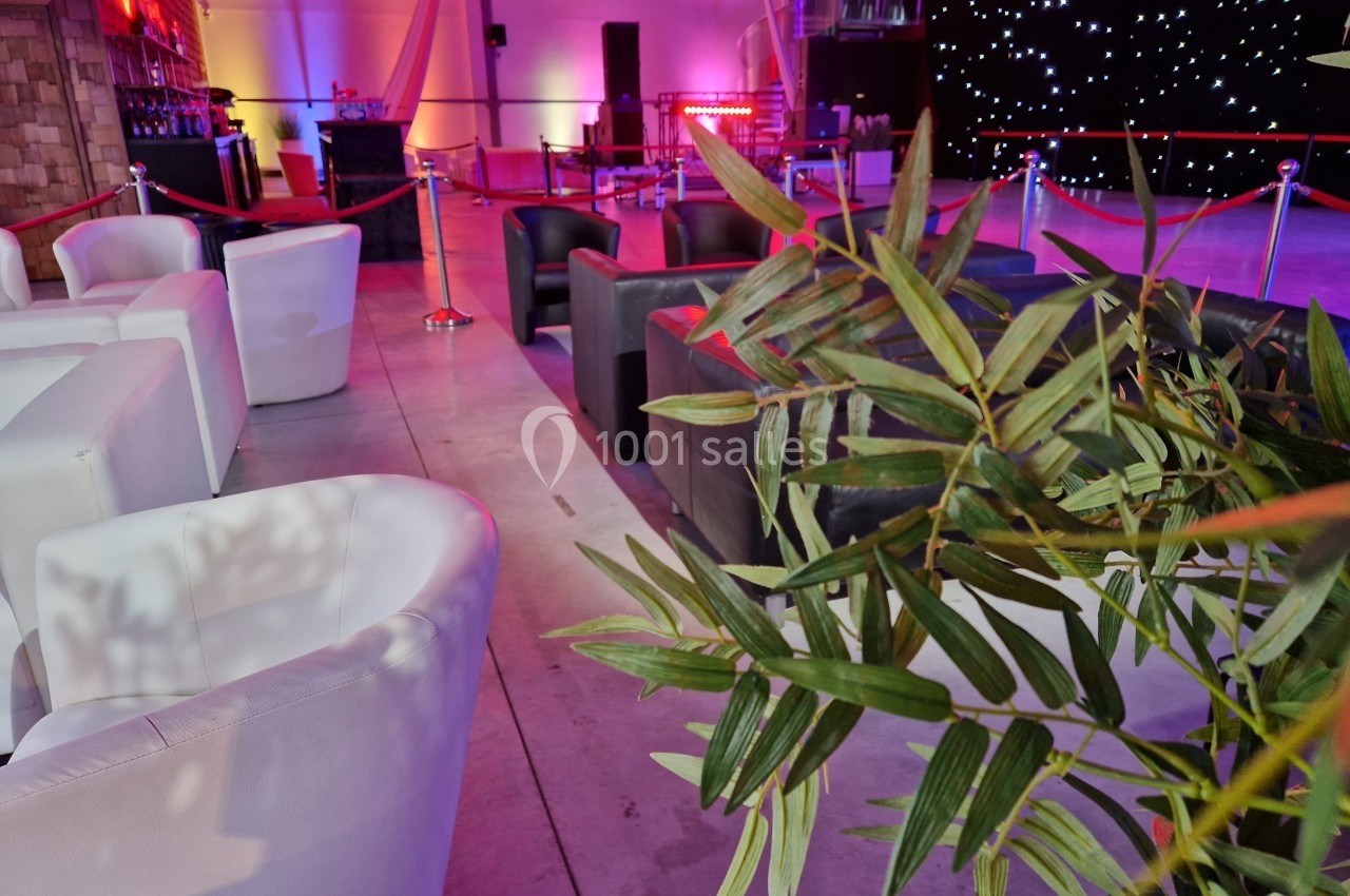 Fauteuils blancs et noirs disposés dans un espace événementiel éclairé avec des lumières colorées et une décoration végétale.