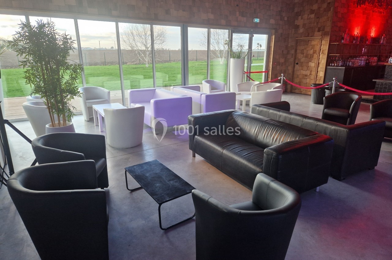 Salon avec fauteuils noirs et blancs, canapé en cuir, table basse, plantes et grande baie vitrée donnant sur un jardin.