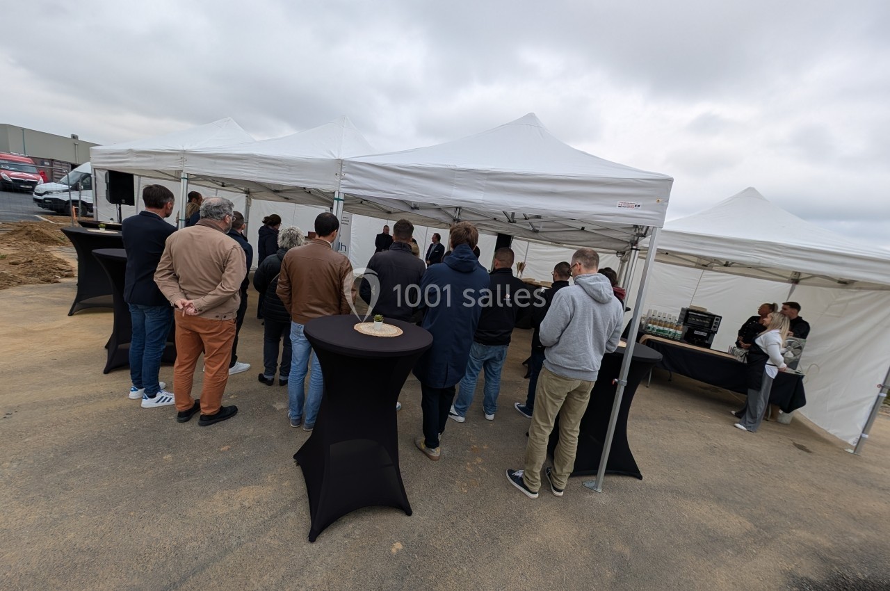 Groupe de personnes debout sous des tentes blanches lors d'un événement en extérieur, avec tables hautes noires.