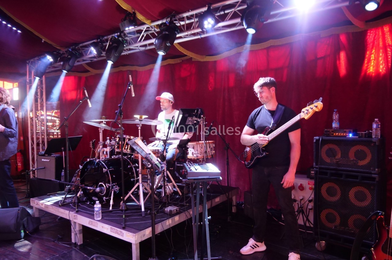 Deux musiciens jouent sur scène, un batteur et un bassiste, sous des projecteurs dans une ambiance de concert.