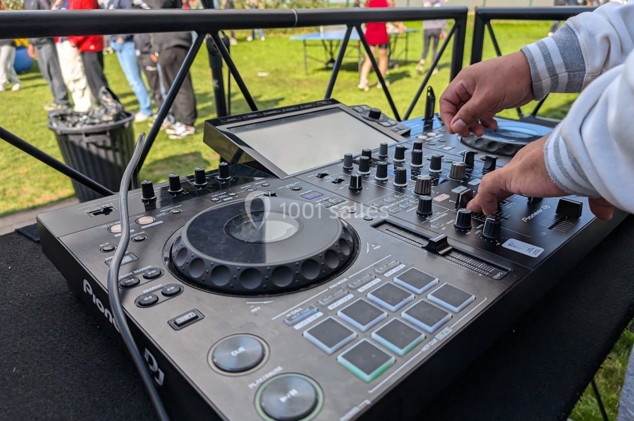 Console de mixage DJ en extérieur, avec des mains ajustant les commandes lors d'un événement en plein air.