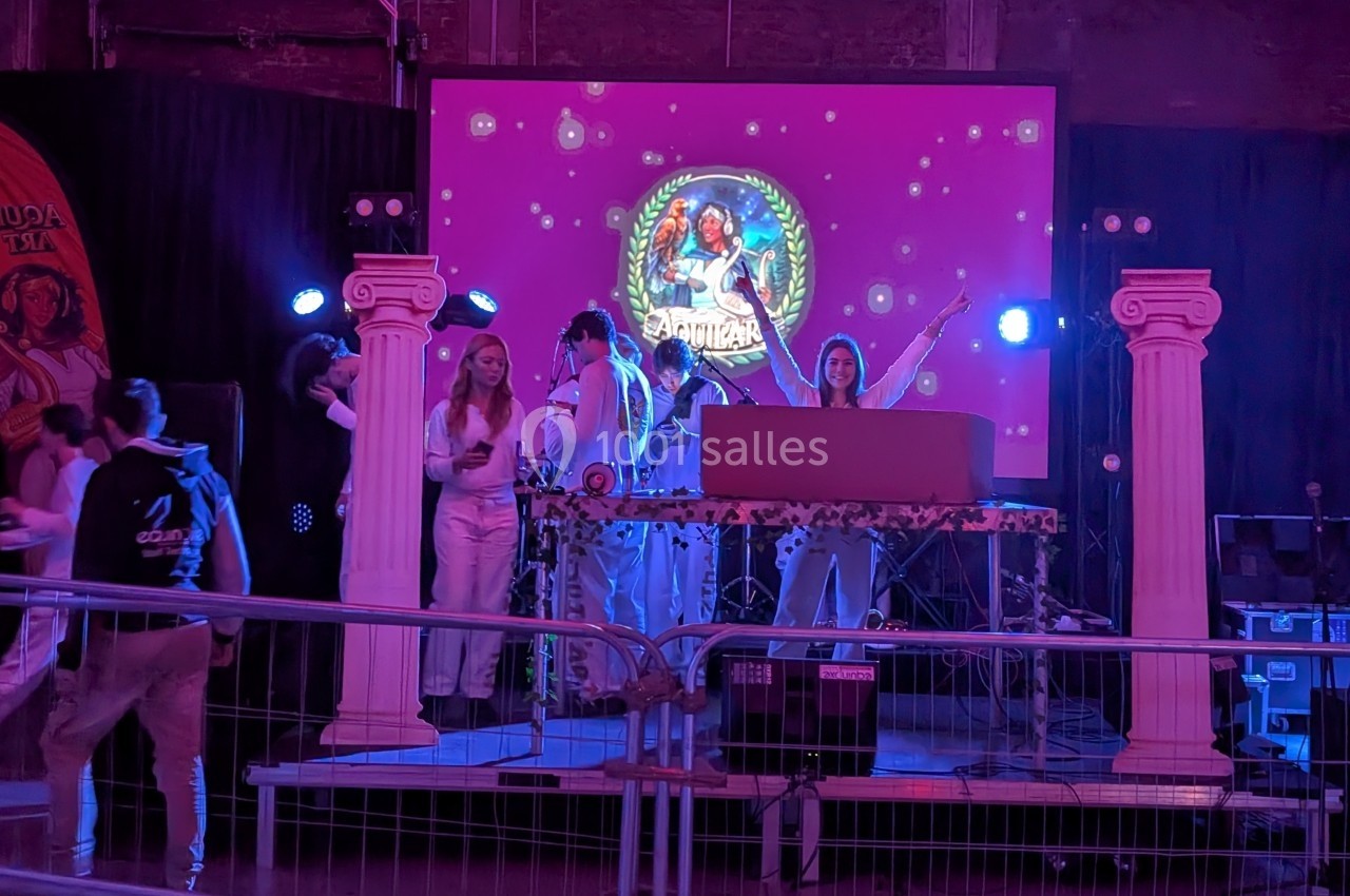 Des personnes en tenue blanche animent une soirée sur une scène décorée de colonnes et d'un écran lumineux.