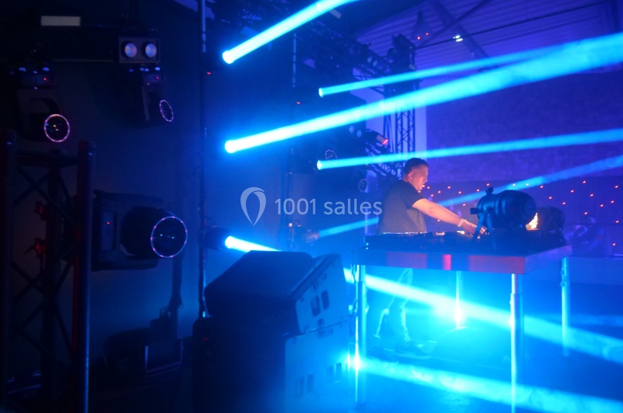 Un DJ mixe sur scène entouré de projecteurs et de faisceaux lumineux bleus dans une ambiance de concert.