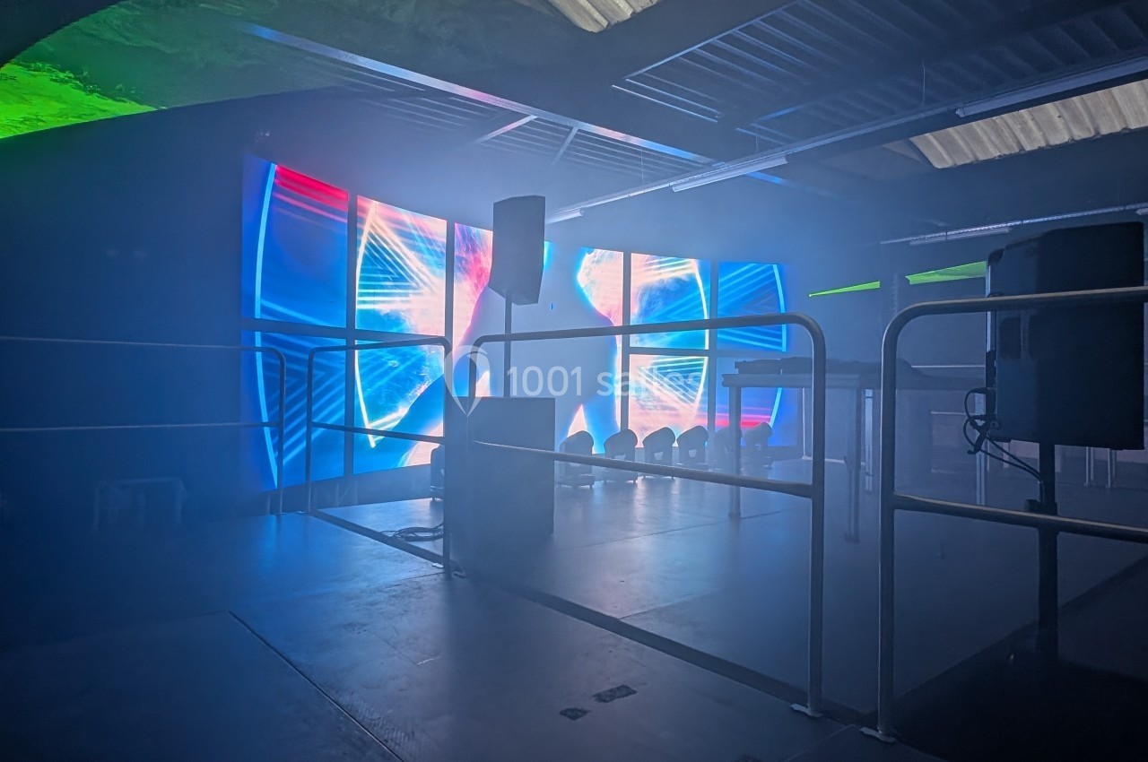 Salle sombre avec écrans lumineux affichant des motifs colorés, entourée de barrières et équipée de haut-parleurs.