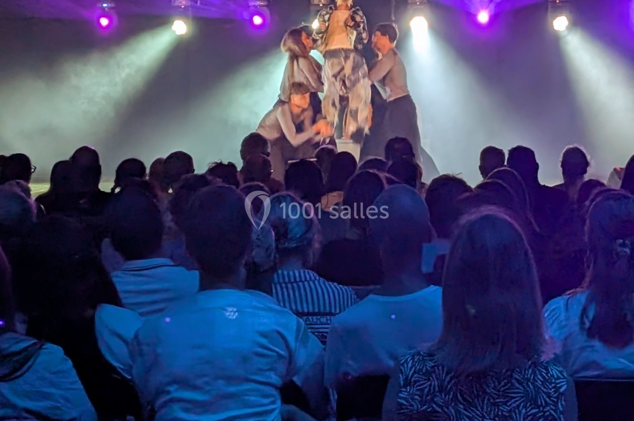 Des artistes sur scène réalisent une performance devant un public dans une salle éclairée par des projecteurs colorés.