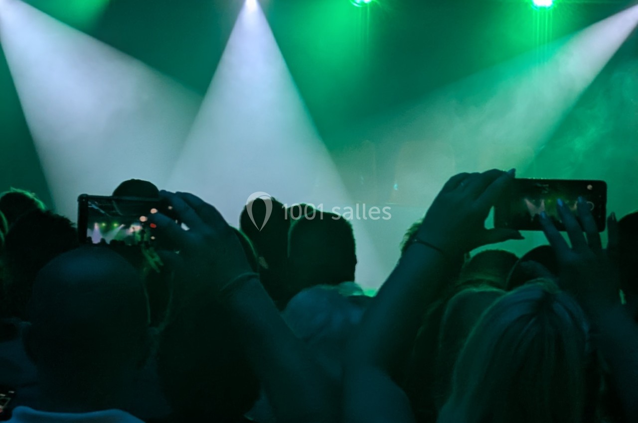 Foule dans une salle de concert sombre, éclairée par des projecteurs verts, avec des spectateurs filmant la scène.