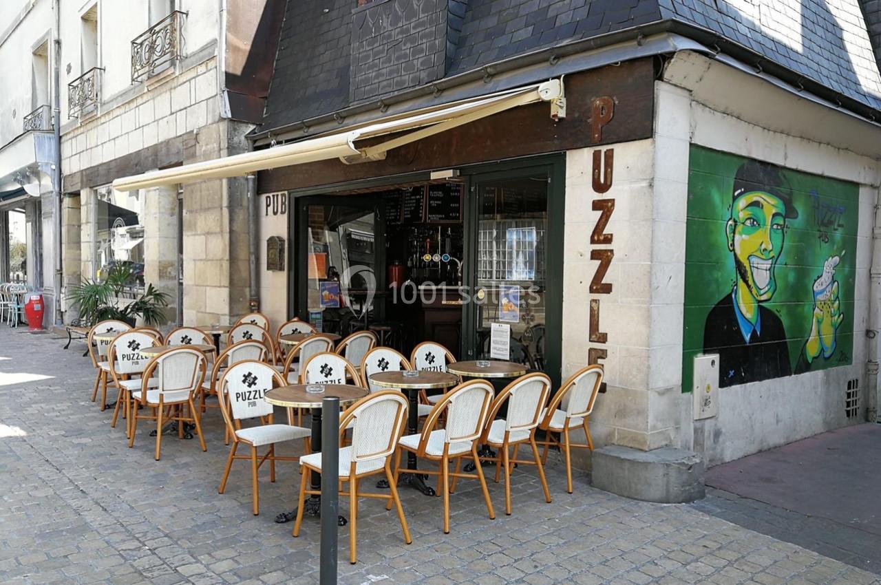 Terrasse d'un café avec des chaises en rotin disposées devant une façade ornée d'une fresque colorée.