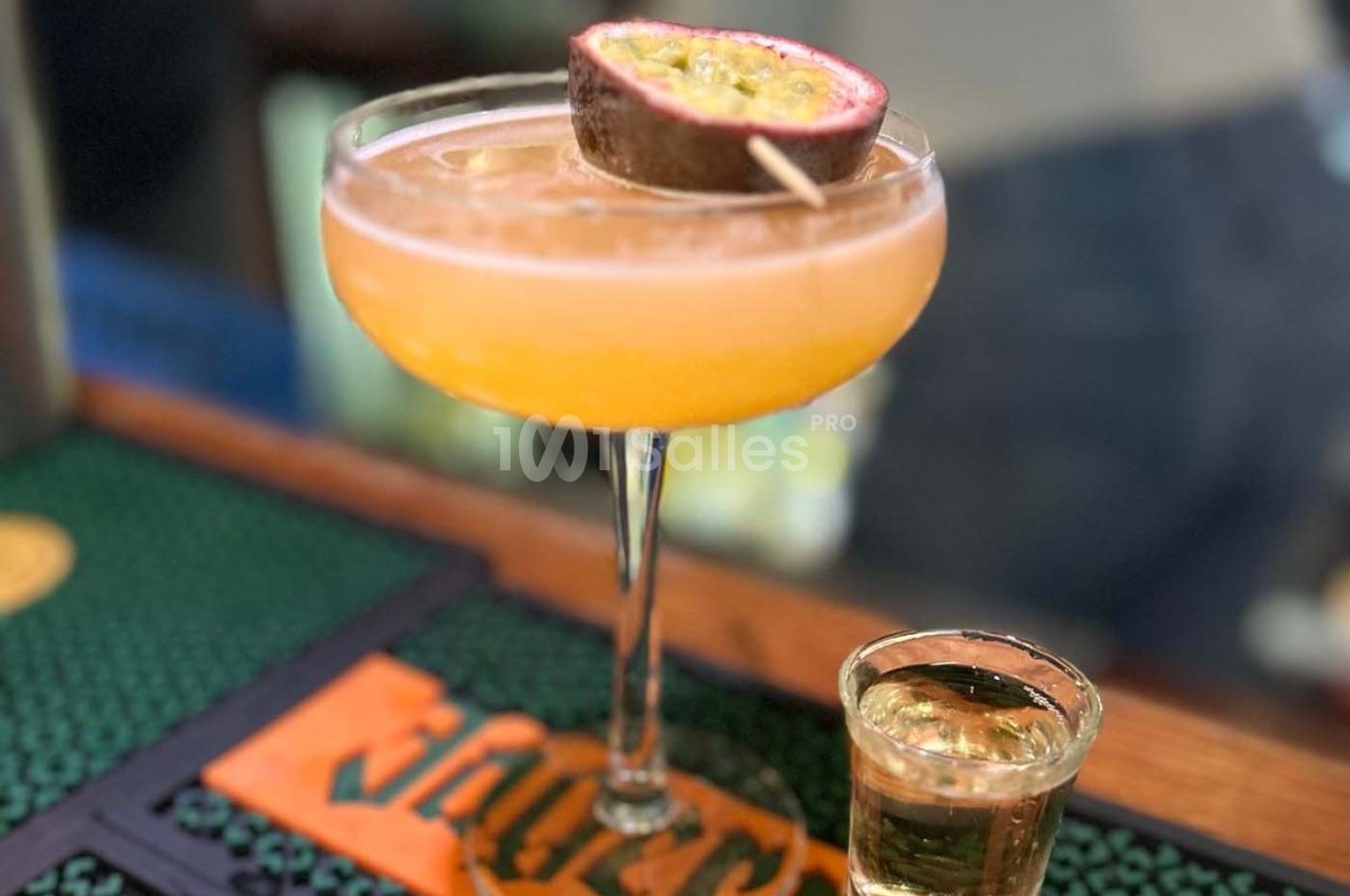 Cocktail orange servi dans une coupe avec un demi-fruit de la passion en garniture, accompagné d'un verre de liqueur.