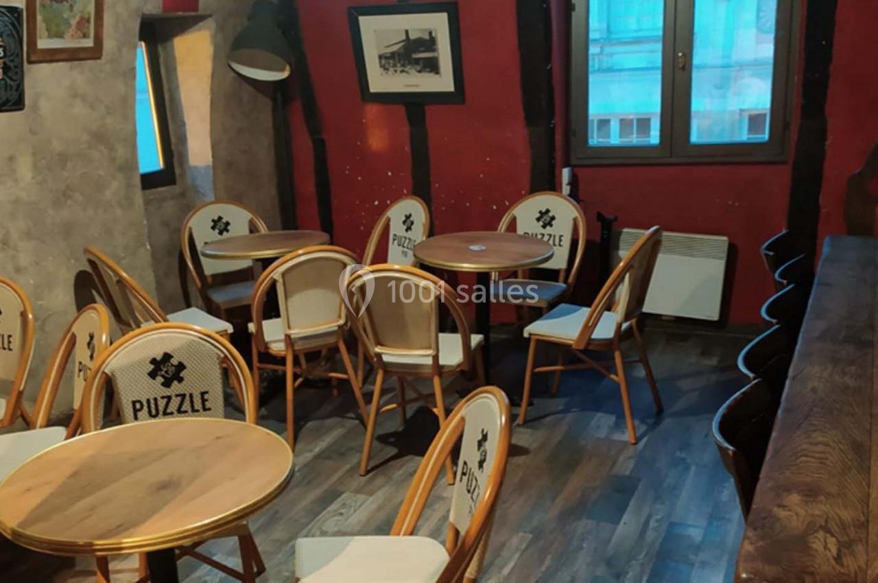 Salle de café avec des tables rondes, des chaises en bois et un décor intérieur chaleureux aux murs rouges et beige.