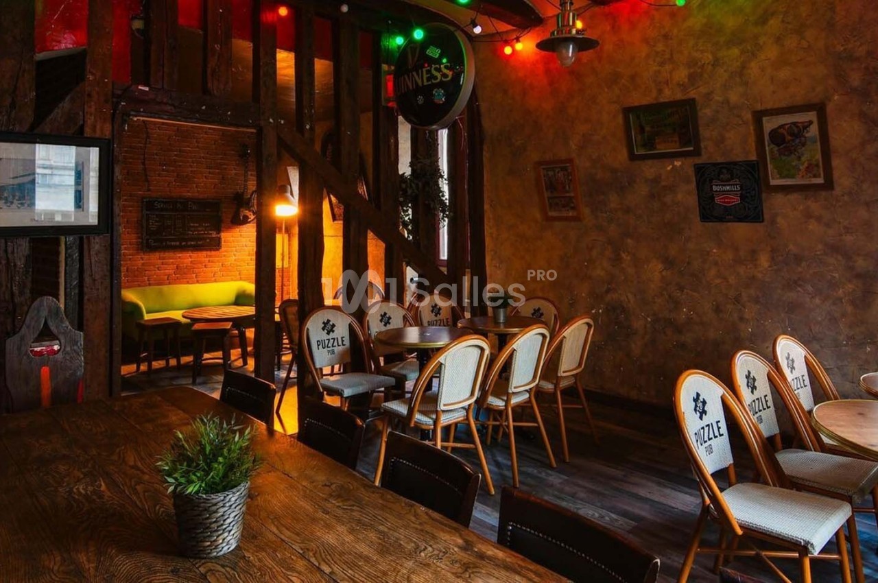 Salle chaleureuse avec murs en bois et briques, éclairage tamisé, tables en bois et chaises disposées autour.
