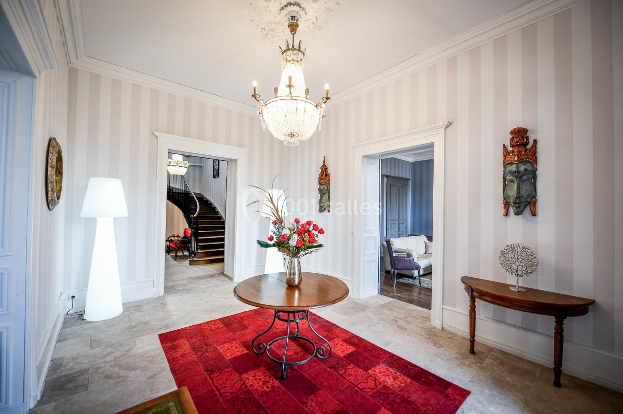 Entrée lumineuse avec un tapis rouge, table ronde décorée de fleurs, escalier en bois et murs à rayures.