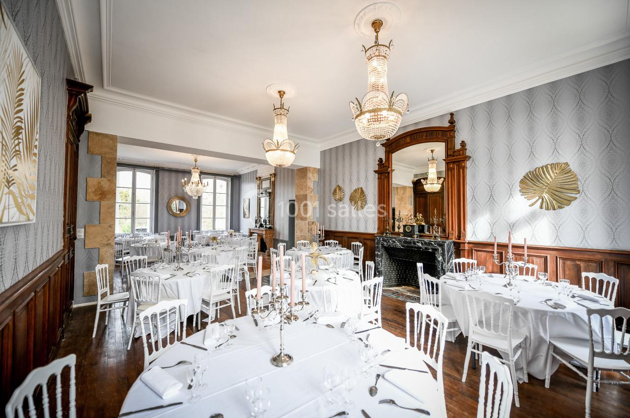 Salle de réception élégante avec tables rondes dressées, chandeliers et décorations murales dorées.
