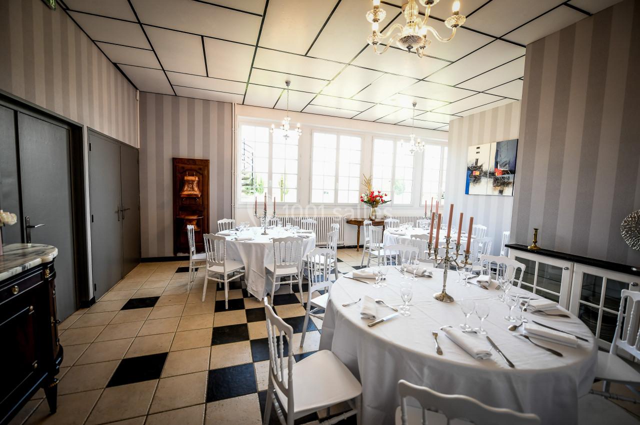 Salle de réception lumineuse avec tables rondes dressées, chaises blanches et décoration élégante.