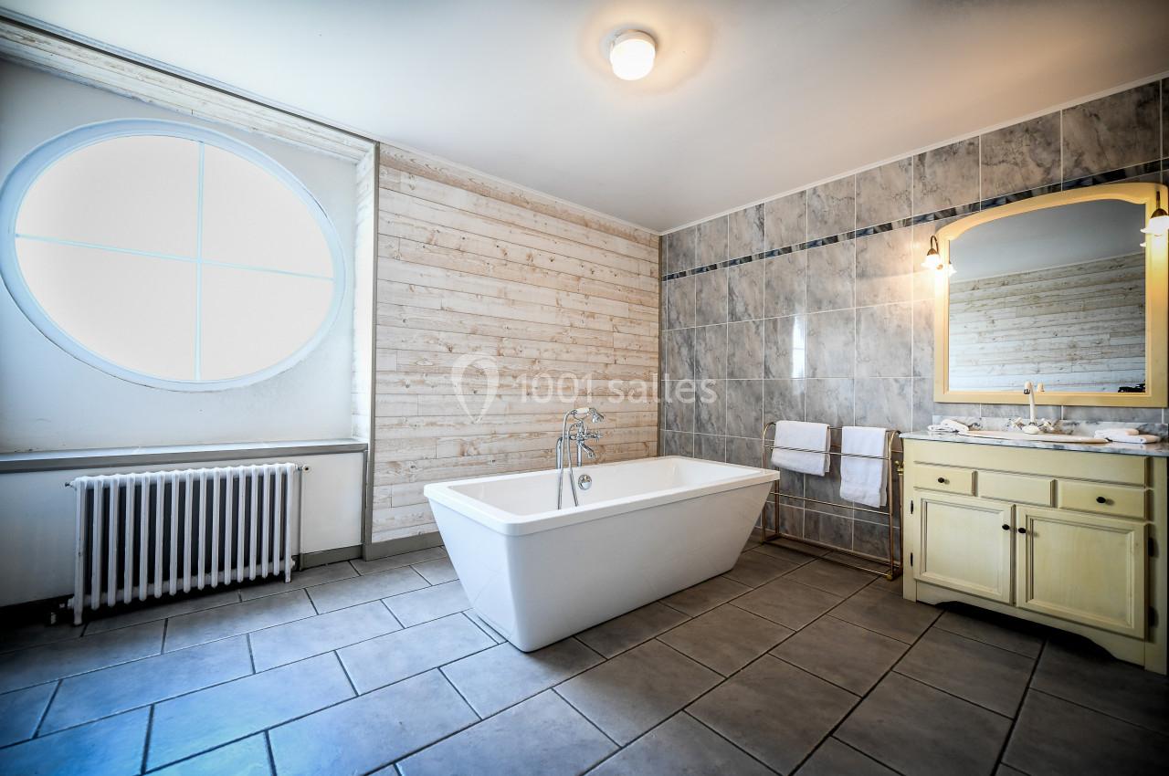 Salle de bain lumineuse avec baignoire blanche, mur en bois clair, carrelage gris et meuble lavabo jaune.