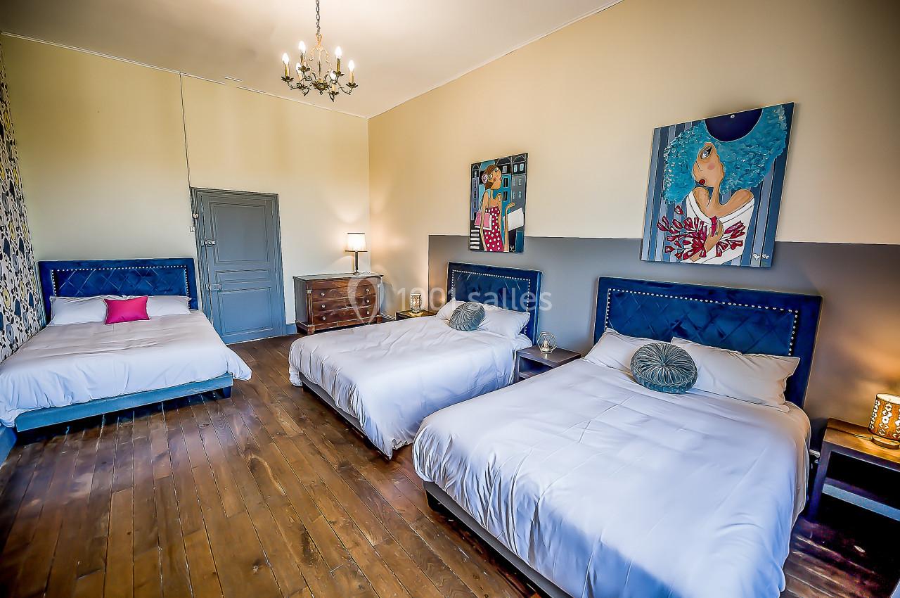 Chambre spacieuse avec trois lits, parquet en bois, murs décorés et éclairage par un lustre.