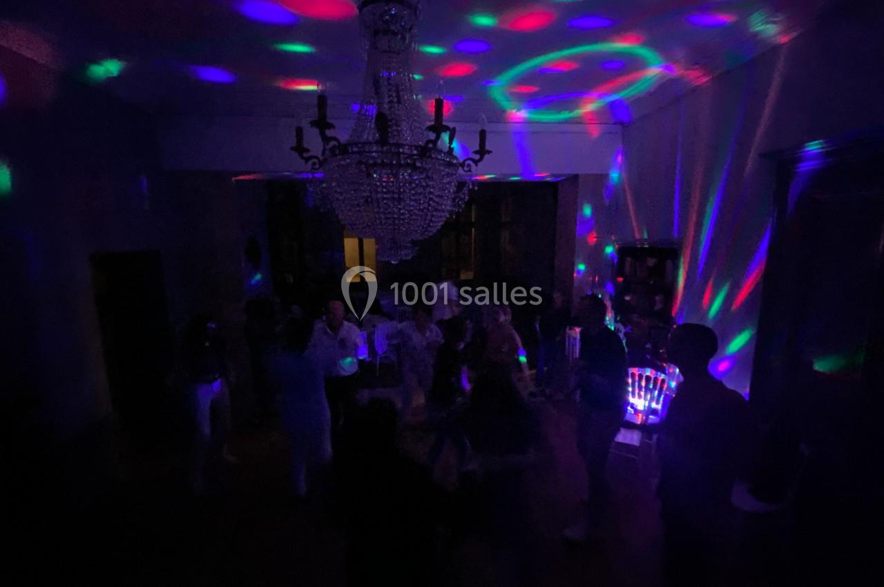 Personnes dansant dans une pièce sombre éclairée par des lumières colorées et un grand lustre central.