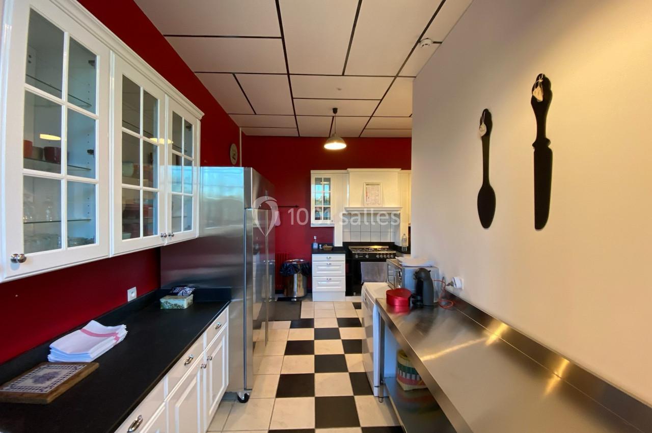 Cuisine moderne avec murs rouges, meubles blancs, plan de travail en inox et sol en damier noir et blanc.