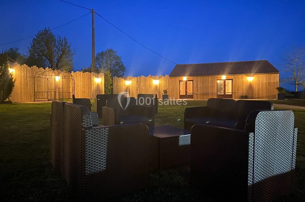 Mobilier de jardin en rotin disposé en cercle sur une pelouse, éclairé par des lumières extérieures au crépuscule.