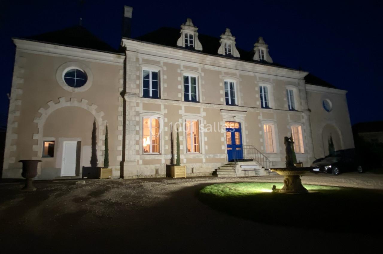 Façade d'un bâtiment ancien éclairé la nuit, avec des fenêtres illuminées et une fontaine au premier plan.