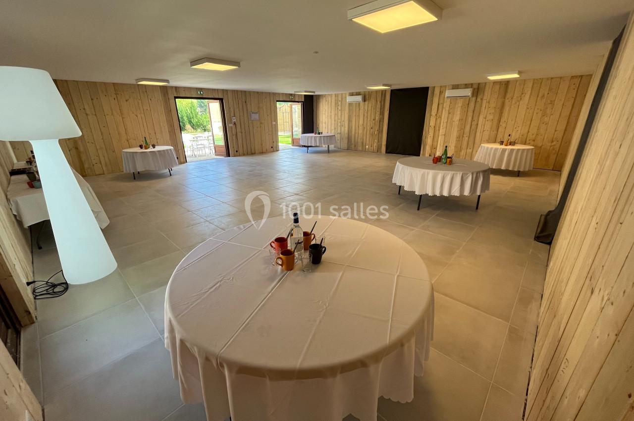 Salle lumineuse avec murs en bois, tables rondes nappées blanches et vue sur un espace extérieur verdoyant.