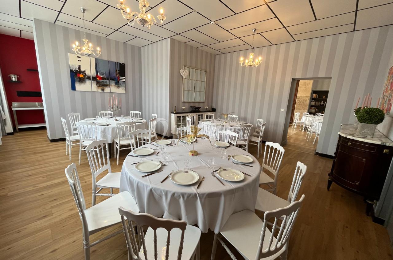 Salle de réception élégante avec tables rondes dressées, chaises blanches et lustres suspendus.