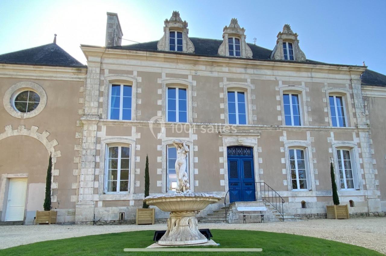 Façade d'un manoir en pierre avec toit en ardoise, fenêtres symétriques et une fontaine sur une pelouse au premier plan.