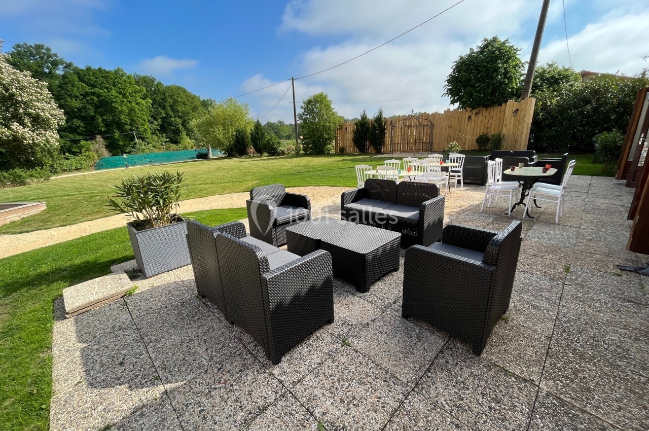 Salon de jardin en résine tressée sur une terrasse en pierre, entouré d'une pelouse et d'arbres sous un ciel dégagé.