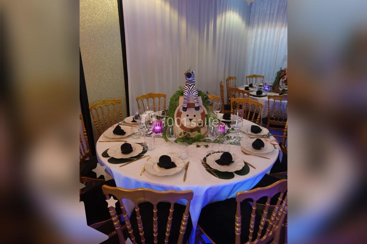 Table ronde décorée sur le thème safari avec centre de table lion, serviettes noires pliées et chaises dorées.