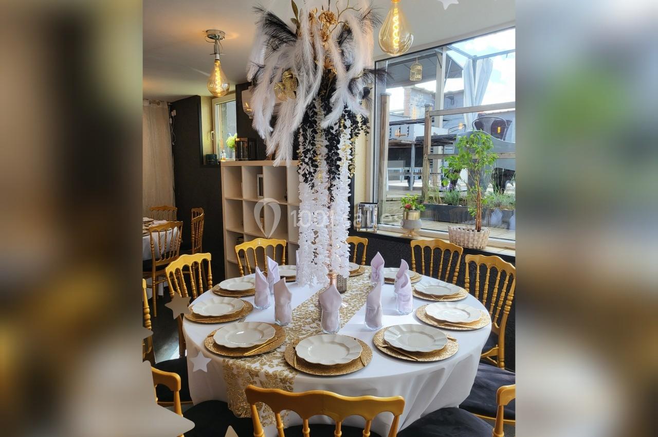 Table ronde élégamment dressée avec une décoration centrale ornée de plumes noires et blanches, dans une salle lumineuse.