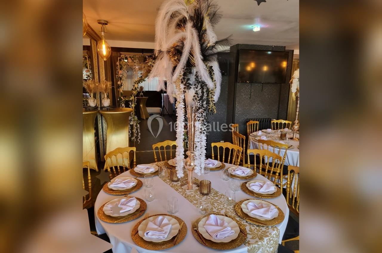 Table ronde élégamment dressée avec nappes dorées, serviettes pliées, assiettes décoratives et centre de table floral.