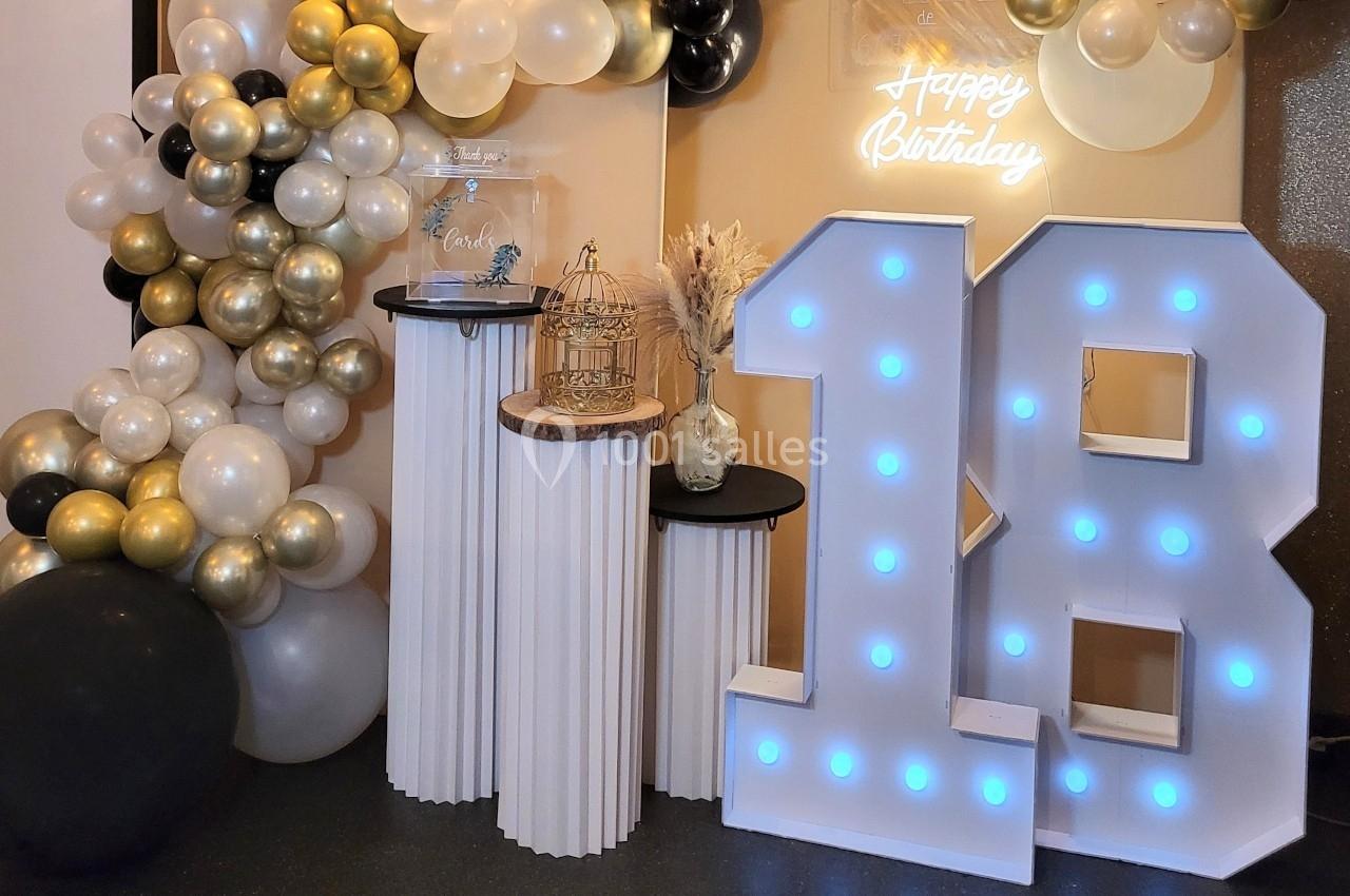 Décoration d'anniversaire avec ballons dorés, blancs et noirs, chiffres lumineux ’18’ et éléments décoratifs sur des…