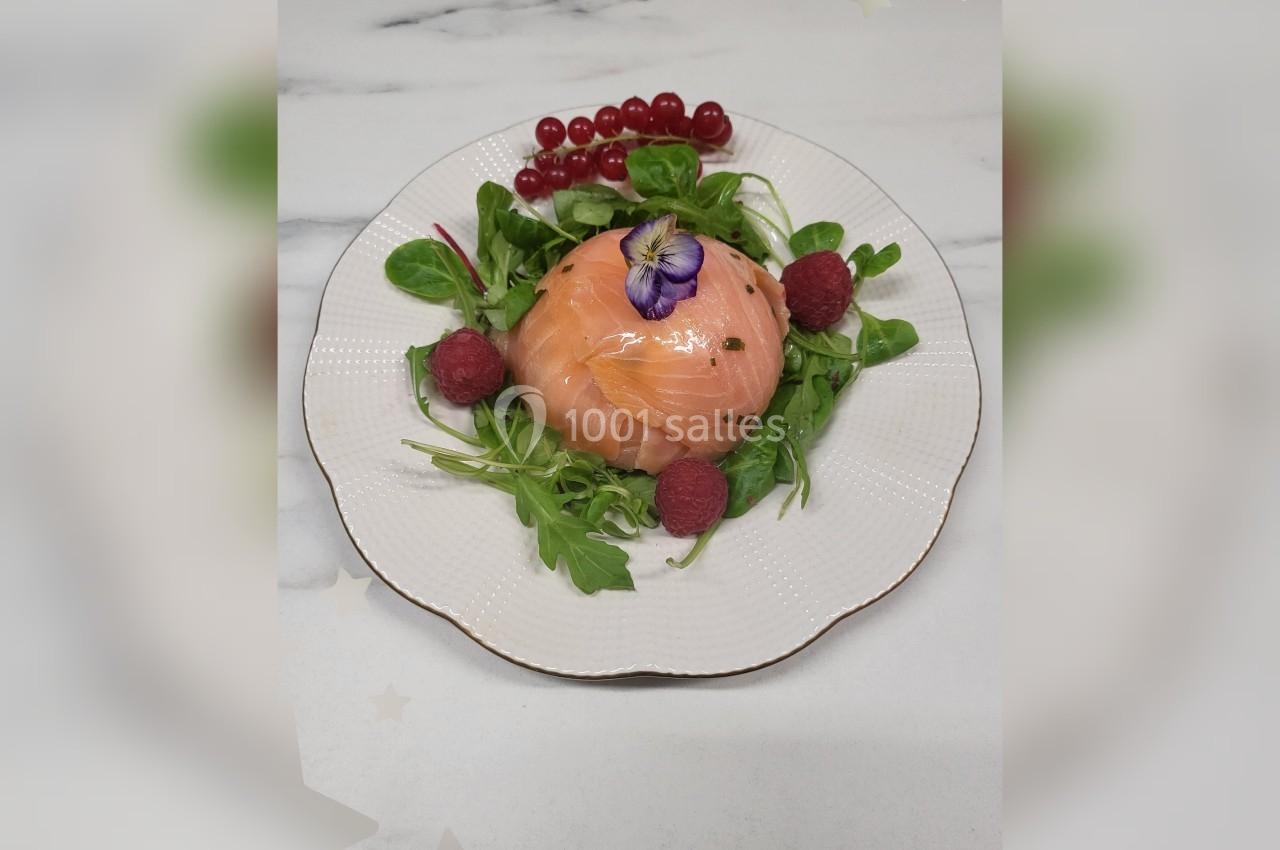 Assiette de saumon fumé en dôme sur un lit de salade, décorée de framboises, groseilles et une fleur comestible.