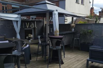 Miniature Location salle Mouscron (Hainaut) - Au Festival de Mouscron  #57 Terrasse en bois avec fauteuils, pergola à rideaux blancs, plantes en pot et mur en briques en arrière-plan.