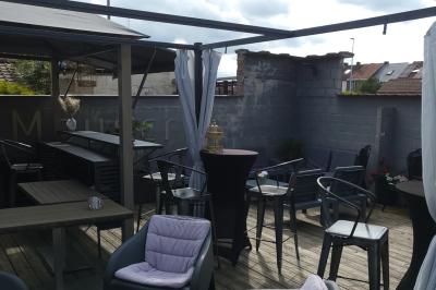 Miniature Location salle Mouscron (Hainaut) - Au Festival de Mouscron  #59 Terrasse en bois avec fauteuils, pergola à rideaux blancs, plantes en pot et mur en briques en arrière-plan.