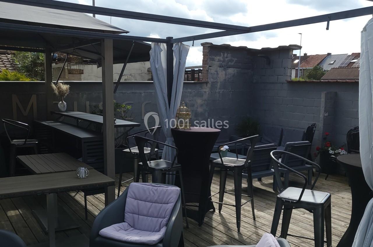 Terrasse en bois aménagée avec des tables, chaises et parasols, entourée de murs gris et partiellement couverte.