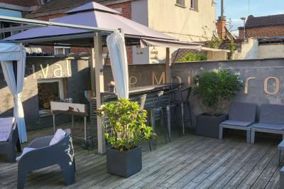 Miniature Location salle Mouscron (Hainaut) - Au Festival de Mouscron  #63 Terrasse en bois avec fauteuils, pergola à rideaux blancs, plantes en pot et mur en briques en arrière-plan.