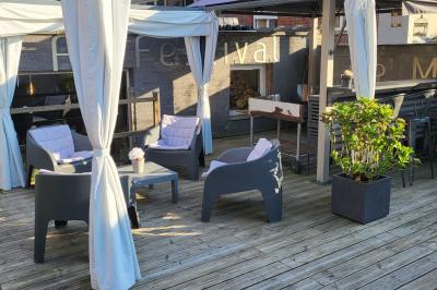 Miniature Location salle Mouscron (Hainaut) - Au Festival de Mouscron  #64 Terrasse en bois avec fauteuils, pergola à rideaux blancs, plantes en pot et mur en briques en arrière-plan.