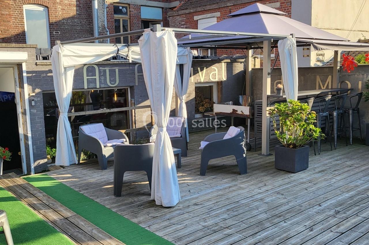 Terrasse en bois avec fauteuils, pergola à rideaux blancs, plantes en pot et mur en briques en arrière-plan.