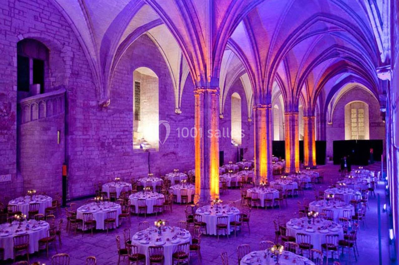Salle voûtée illuminée en violet et orange, aménagée avec des tables rondes dressées pour un événement.