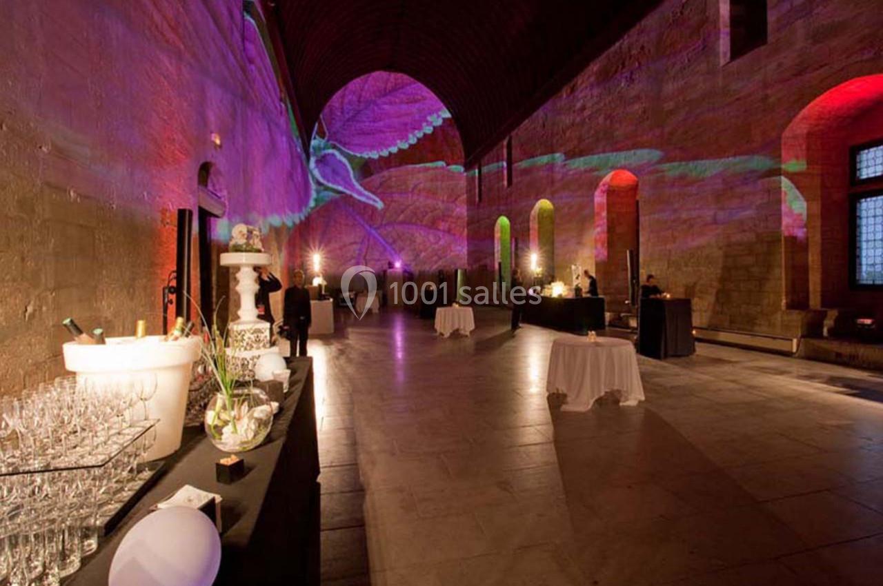 Salle voûtée éclairée par des projections colorées, avec tables dressées et buffet installé sur la gauche.