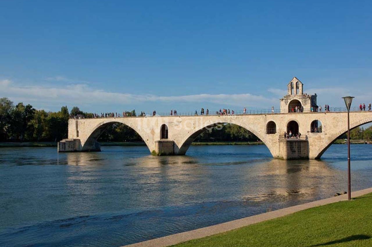 Vue d'un pont en pierre partiellement détruit traversant une rivière, avec des visiteurs et un ciel dégagé.