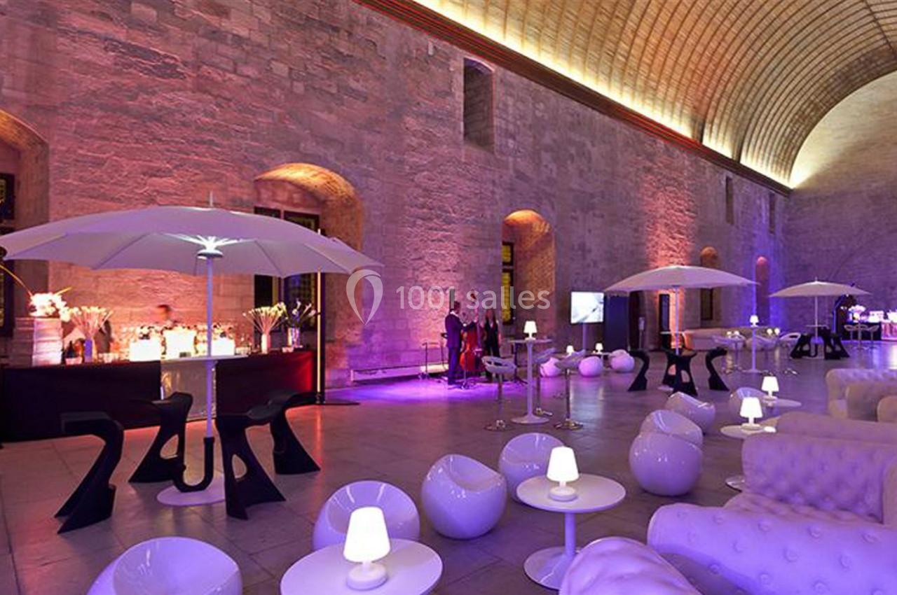 Salle voûtée éclairée de lumières colorées, aménagée avec des fauteuils modernes, des parasols et un bar.