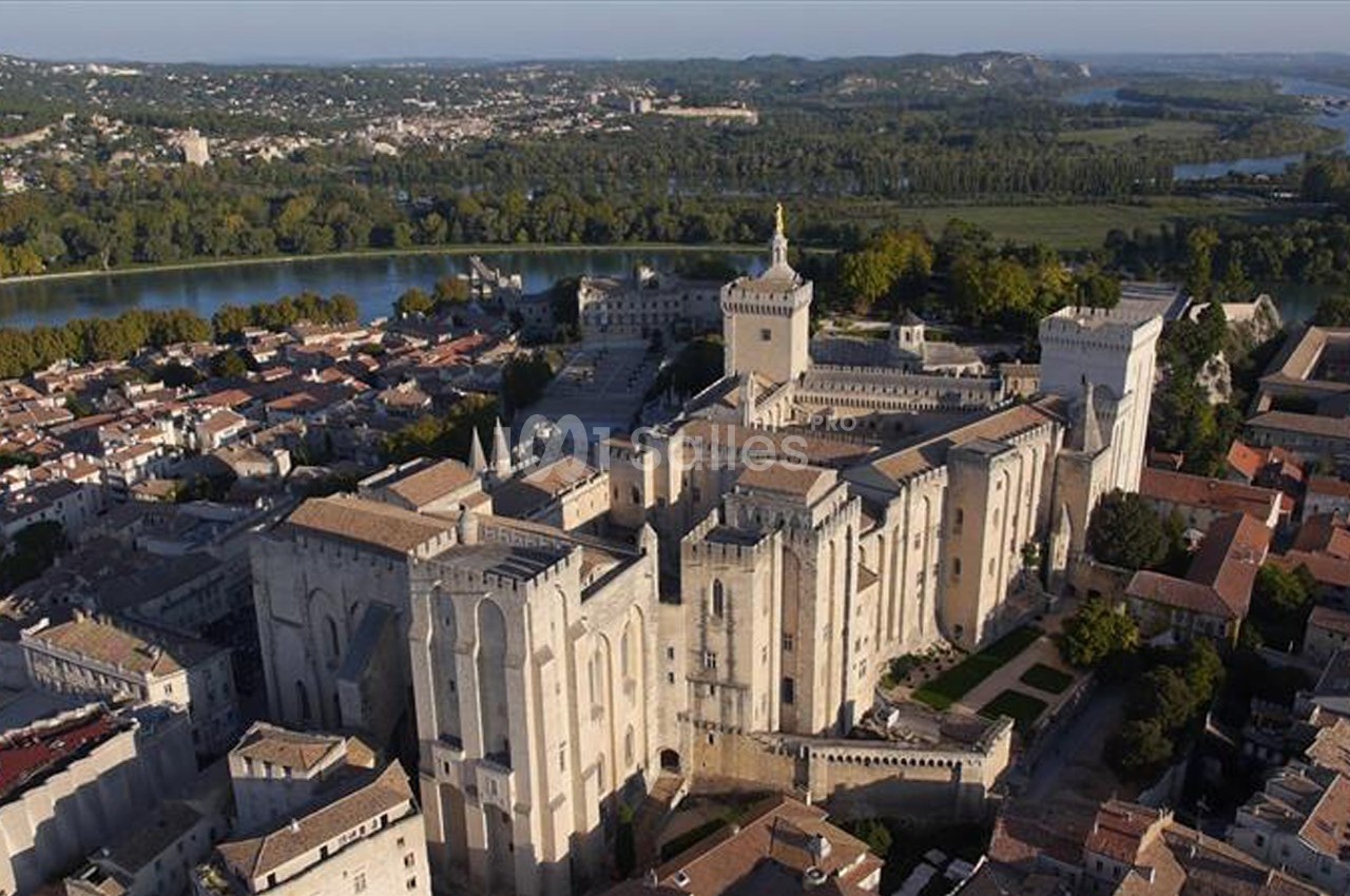 Vue aérienne du Palais des Papes à Avignon, entouré de bâtiments historiques et bordé par le Rhône.