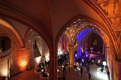 Vue nocturne d'un jardin avec des invités rassemblés lors d'un événement, éclairé par des lumières chaleureuses.