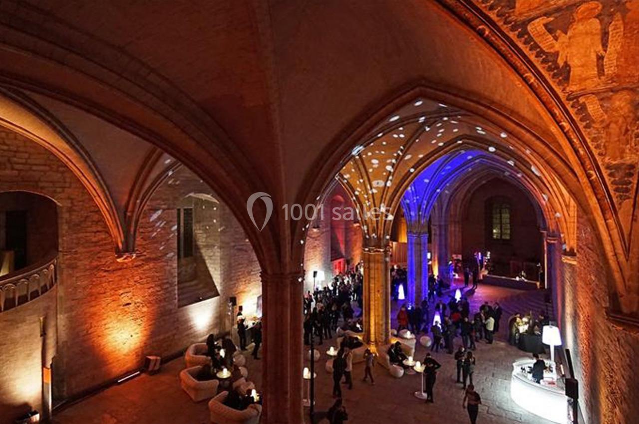 Vue intérieure d'une salle gothique avec des voûtes éclairées de lumières colorées et des invités rassemblés.