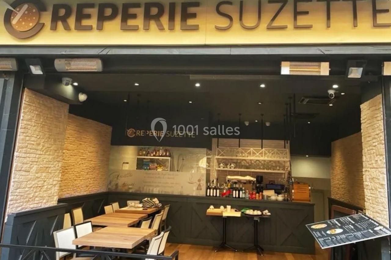 Façade d'une crêperie avec terrasse en bois, tables et chaises, et un comptoir visible à l'intérieur.