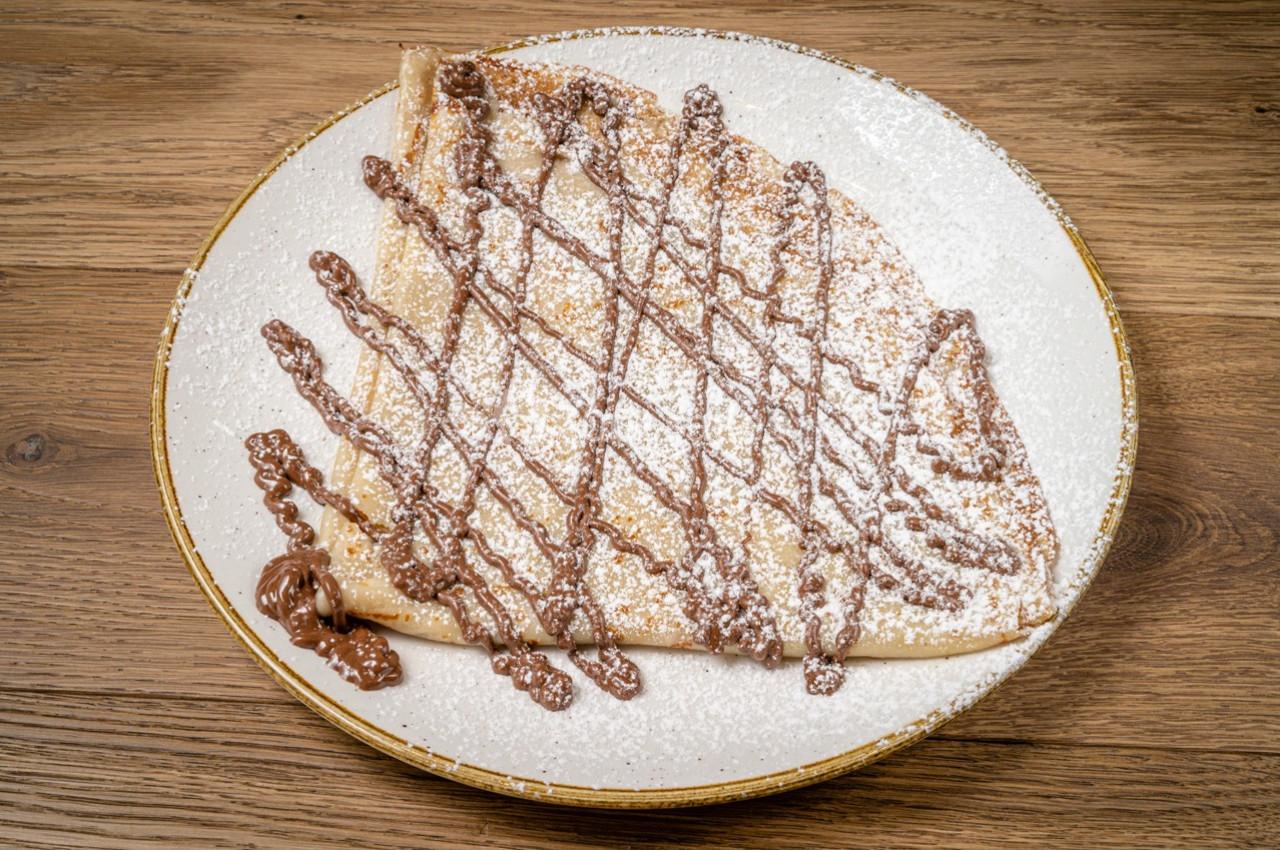 Crêpe pliée garnie de chocolat fondu et saupoudrée de sucre glace, servie sur une assiette blanche.